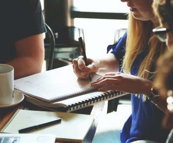 Group of people sat around a table with one person writing notes in a notebook