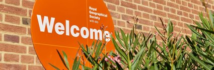 A circular orange sign reading Welcome, next to a green plant with pink flowers