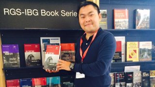 A man in front of a bookstand holding up a book.