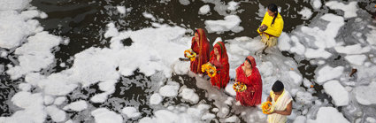 A group of people wearing traditional Indian clothing standing in a river while performing a religious ritual.
