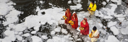 A group of people wearing traditional Indian clothing standing in a river while performing a religious ritual.