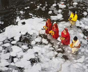 A group of people wearing traditional Indian clothing standing in a river while performing a religious ritual.