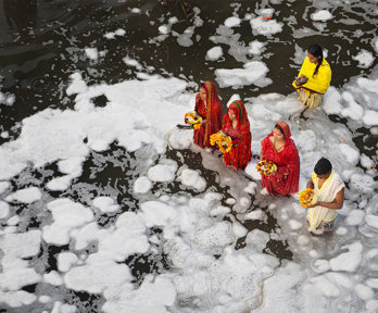 A group of people wearing traditional Indian clothing standing in a river while performing a religious ritual.