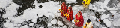 A group of people wearing traditional Indian clothing standing in a river while performing a religious ritual.