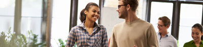 Two coworkers talking and smiling while walking down a modern office.