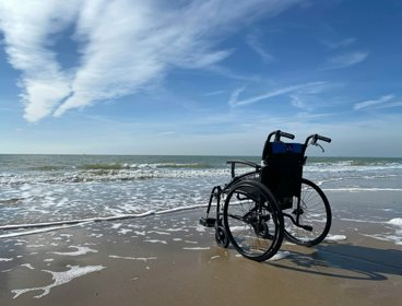 An empty wheelerchair on a sandy beach, facing towards the sea