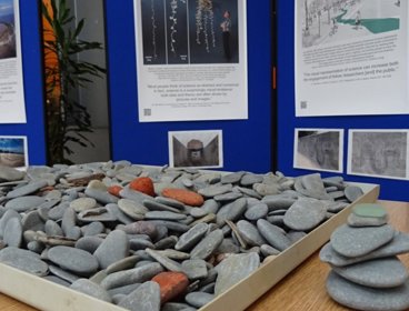 A tray of stones on a wooden table, with posters and display boards behind