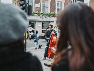 A person playing a double bass on the street with people watching