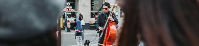 A person playing a double bass on the street with people watching