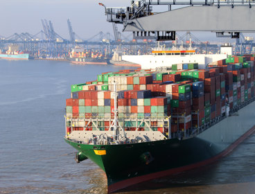 Container ship showing coloured shipping containers piled up, with cranes in the background