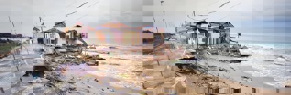 A damaged house and road by the coast. Rubble lays on the beach.