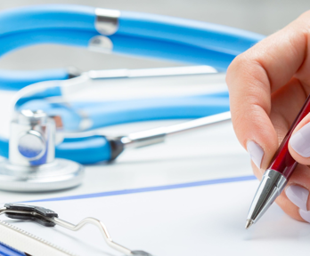 A person uses a pen to write on a peice of paper attached to a clip board. a stethoscope sits on the table next to the paper and clip board