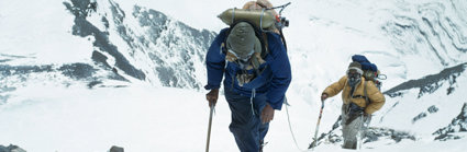 Two mountaineers in full winter tracking gear walking a snow covered mountain.