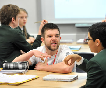 A male geography ambassador crouching down next to a male student, talking to them about geography