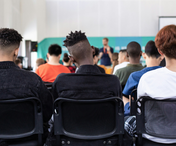 Teenagers sit in a hall listening to a presenter speak