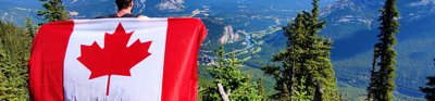 Man standing overlooking a mountain view, holding a Canadian flag