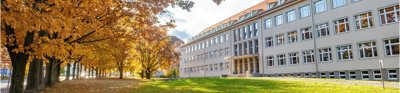 Large stately building fronted by green lawn and deciduous, golden and orange trees.