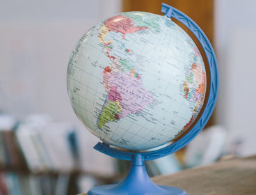 A globe on top of a wooden desk in classroom.