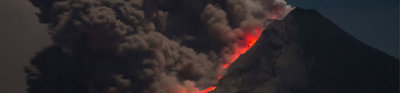 A volcano eruption with large smoke plumes rising into a dark sky and lava flowing down the side of the volcano.