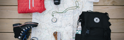 Walking boots, a backpack, compass, folded jacket, digital camera, poloroid camera and note book are all placed on a map
