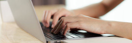 Close up of a person's hands typing on a laptop keyboard.