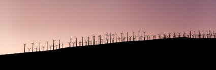 A sillouette of wind farm turbines on a slope with a purple sky