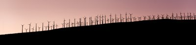 A sillouette of wind farm turbines on a slope with a purple sky