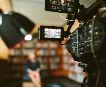 Camera filming person sat on a chair in front of bookcases 