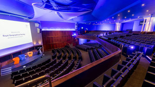 View from the balcony in the Ondaatje Theatre at the Royal Geographical Society. A presentation slide is projected on the screen and says 'Welcome to the Roayl Geographical Society'.