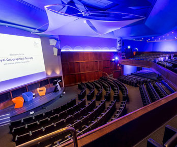 View from the balcony in the Ondaatje Theatre at the Royal Geographical Society. A presentation slide is projected on the screen and says 'Welcome to the Roayl Geographical Society'.