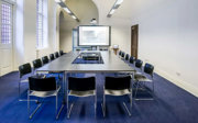 A meeting room setup in boardroom style with a screen at the front.