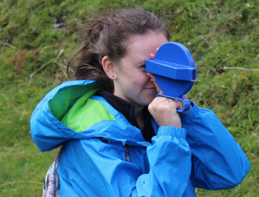 Person wearing blue rain jacket holding geographical equipment outdoors.