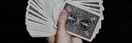 A hand holding a fan of playing cards. The background is black and you cannot see the colourful side of the cards, only the back