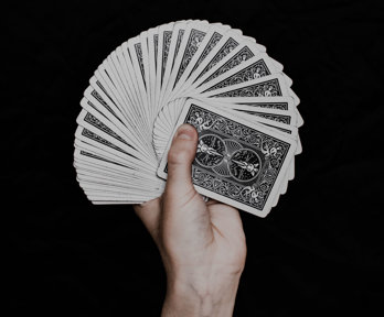 A hand holding a fan of playing cards. The background is black and you cannot see the colourful side of the cards, only the back