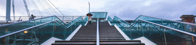 Modern city stairs shot from below. One person is at the top of the stairs, walking down and holding an umbrella. 