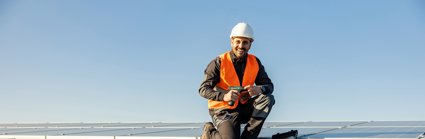 A worker crouching and smiling by some solar panels