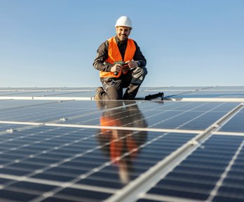 A worker crouching and smiling by some solar panels