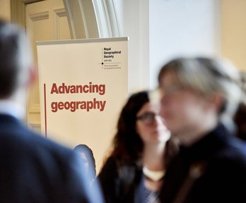 Banner with the text 'Advancing geography' and the Society's logo, with blurred figures in the foreground 