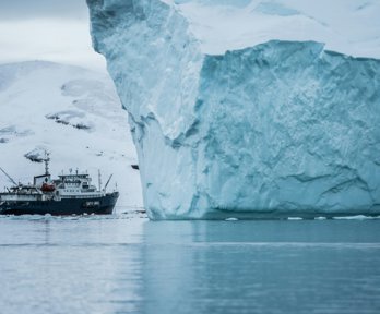 Iceberg with a ship sailing closely next to it.