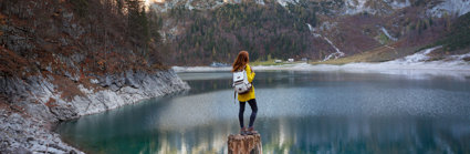 Person standing on broken tree trunk overlooking a lake and mountains.