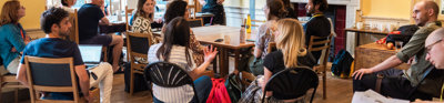 A presenter stands next to a screen with a presentation while listening attentively to an audience member talking.