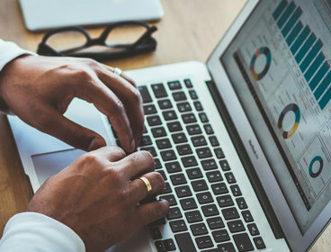 Person typing on a laptop keyboard with graphs on the screen. 