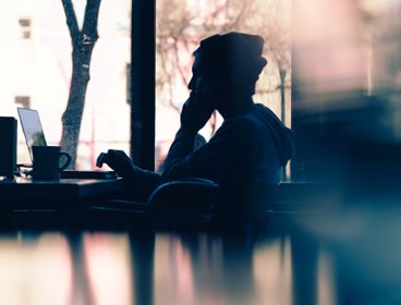 Silhouette of a person sitting in front of a laptop