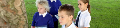 Four children holding maps outside. They are standing in a field of grass and next to a tree.