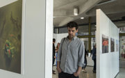 A man in a grey shirt and black trousers standing looking at an image in a photographic exhibition.