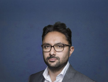 Person with glasses against dark blue background.