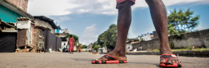 A pair of flip flopped feet, standing ona  road with settlements behind